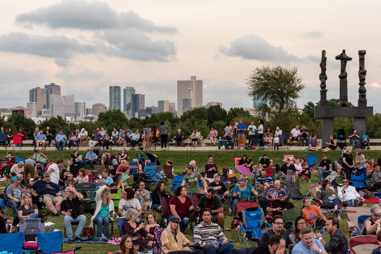A large crowd of people sit and mingle on the grassy lawn in front of the Carter.