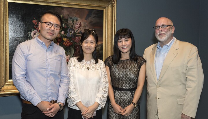 Four people pose in front of an artwork.