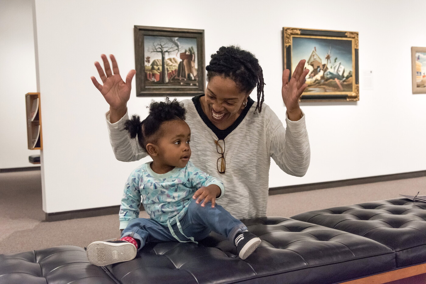 An adult sits on a bench in a Carter gallery with a baby on their lap.