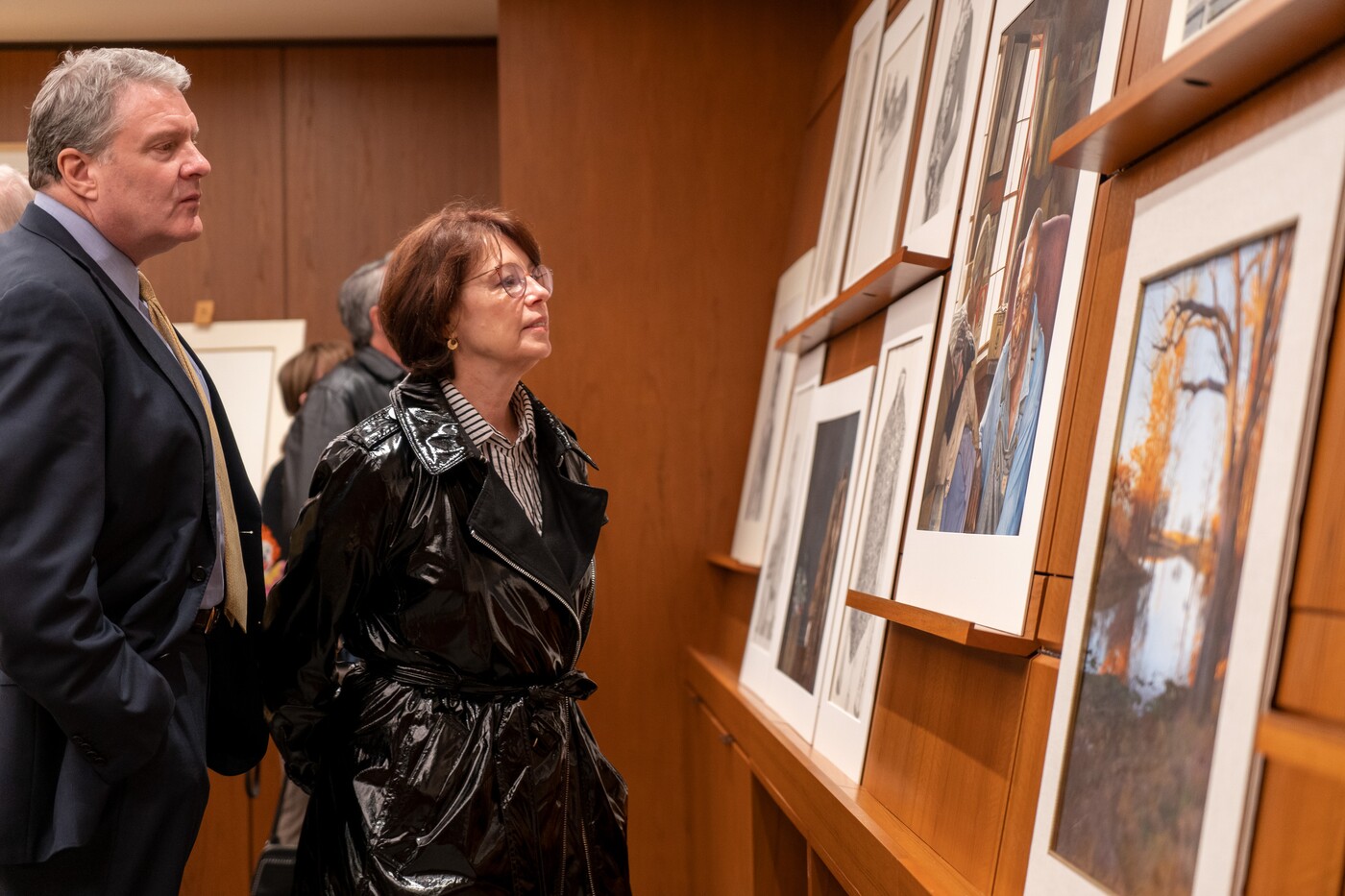 Two middle-aged people, a man and a woman, look closely at artwork displayed on a wall