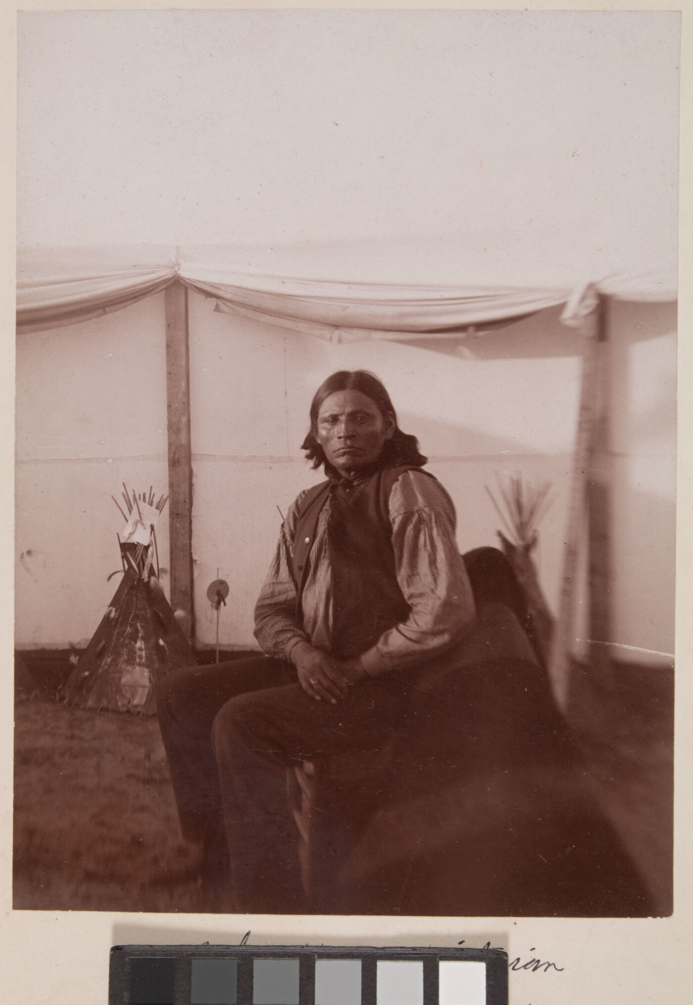 [Anko wearing striped shirt and seated in canvas corral, tipi models in