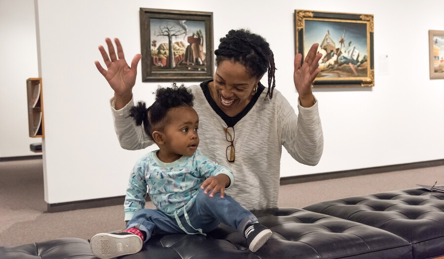 An adult sits on a bench in a Carter gallery with a baby on their lap.