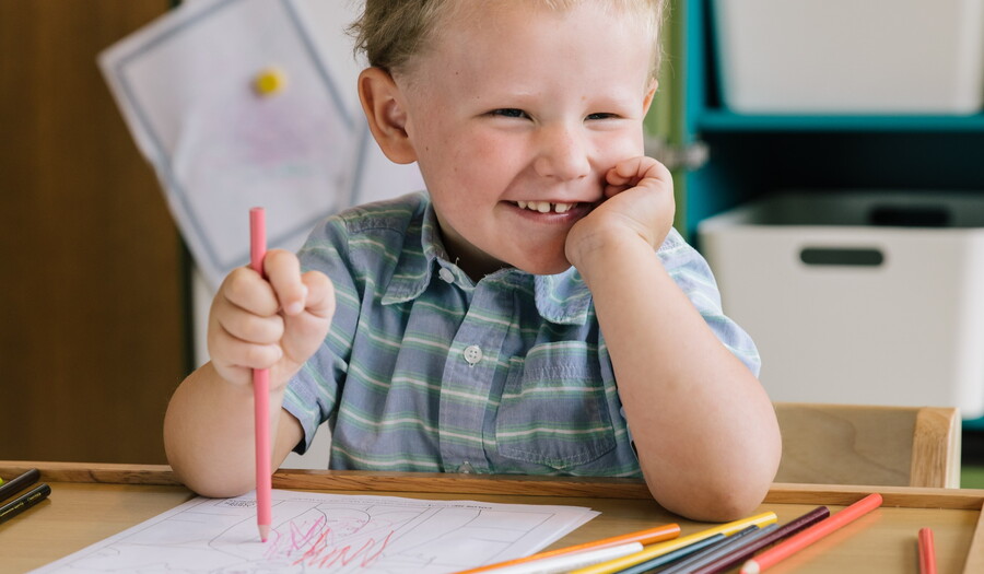 A toddler uses colored pencils to draw on paper.