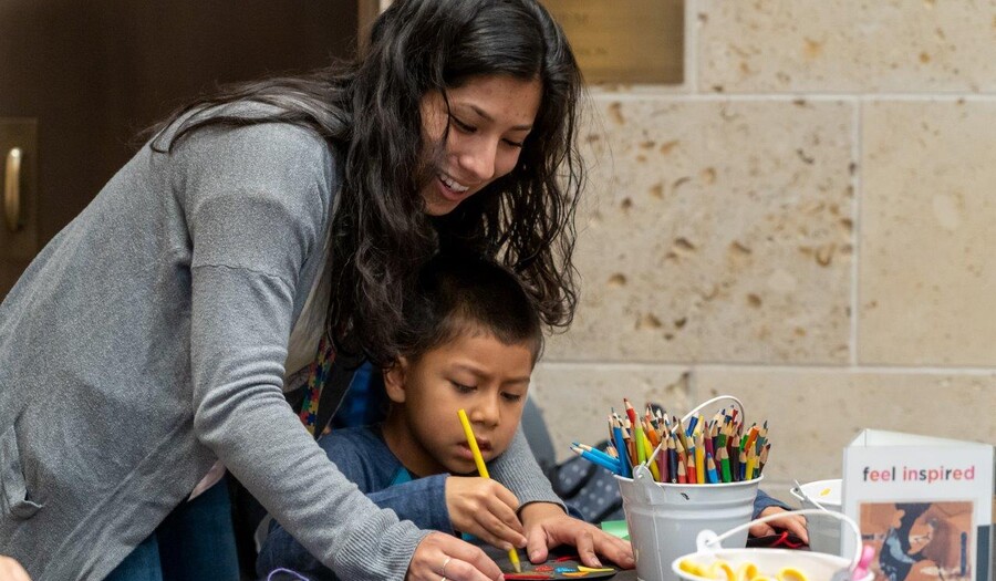 A woman helps a small child who works on an art project.