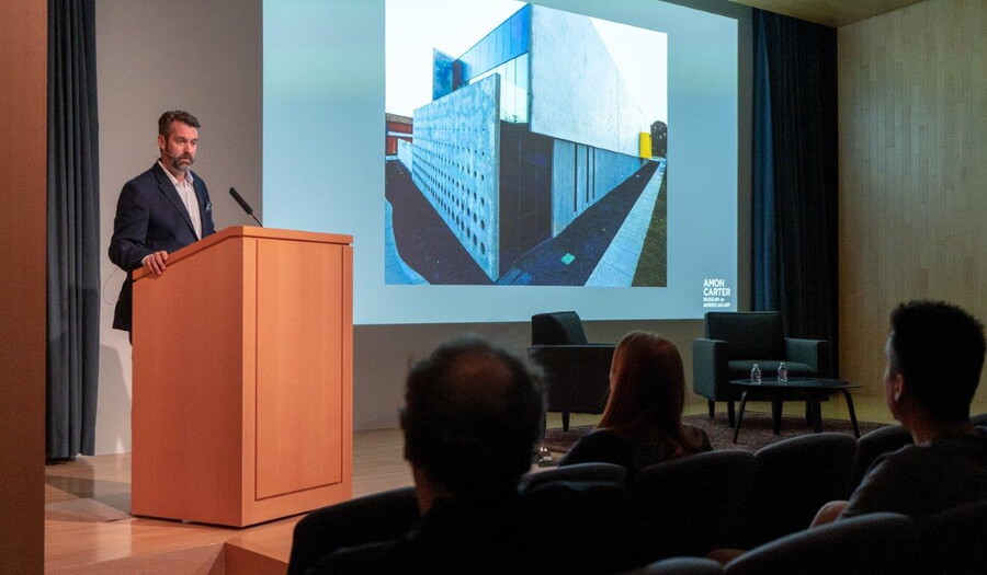 In the Carter's auditorium, a man stands at a podium next to a screen showing artwork.