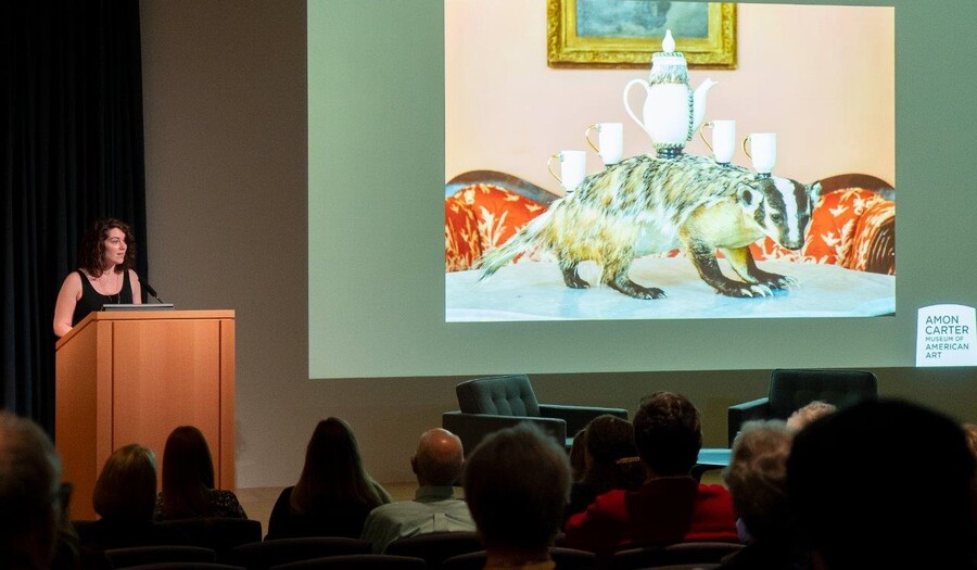 In the Carter's auditorium, a woman stands at a podium next to a screen showing artwork.