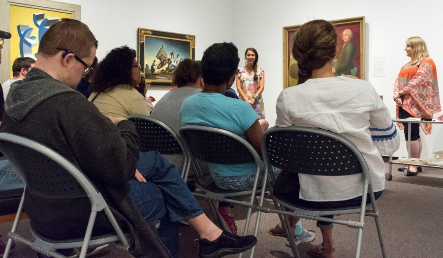 A group of adults sit in a Carter gallery listening to a tour.