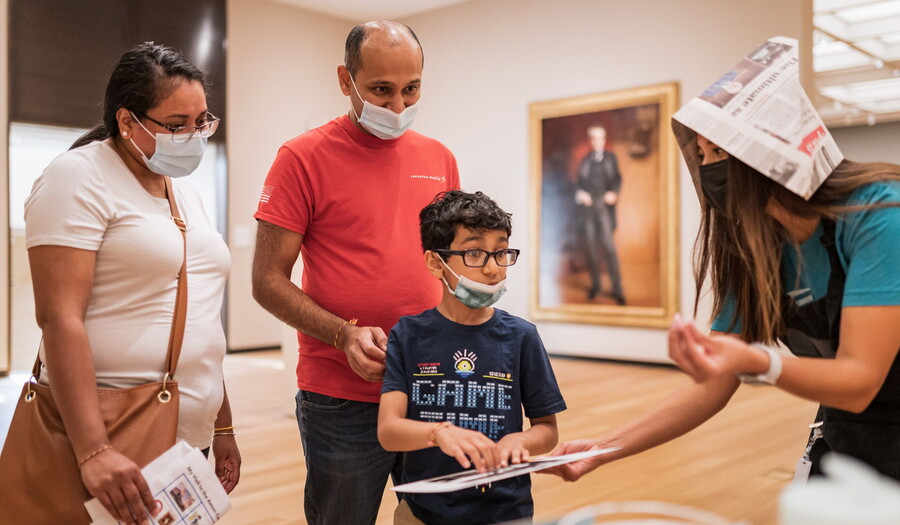A family in a gallery interacts with a Carter educator holding a tablet.