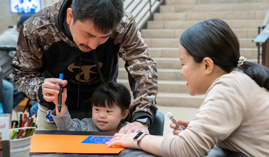 Two adults help a small child make art in the Carter's Atrium.