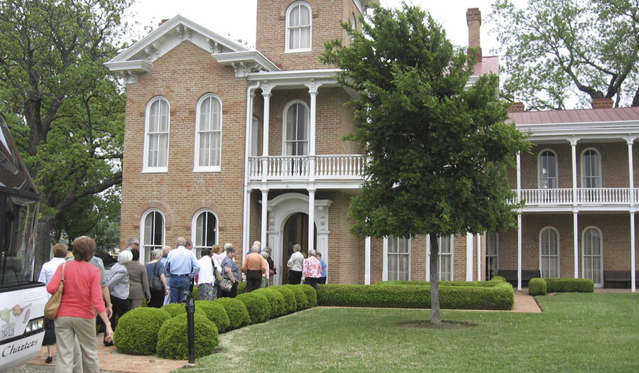 A group of people file into a two-storey brick mansion.