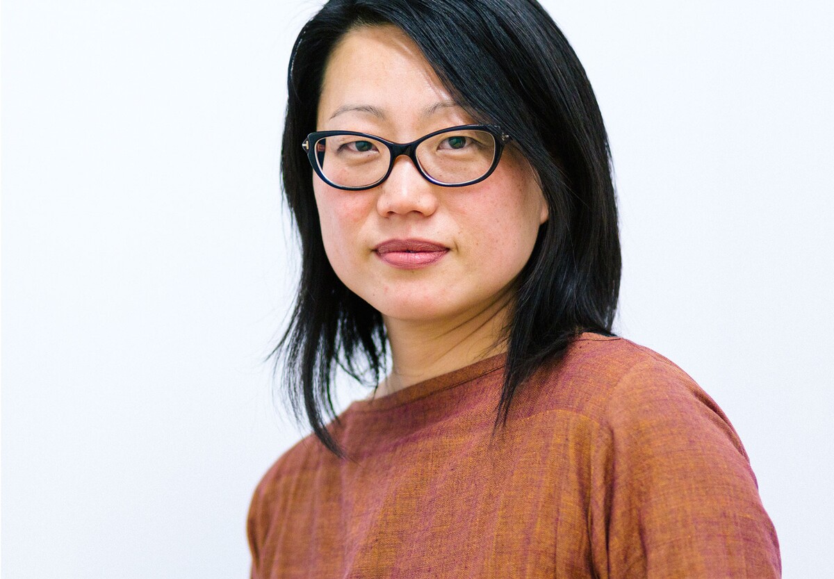 Headshot of a medium-light-skinned woman with Asian features, shoulder length black hair, black-framed glasses, and a rust-colored top