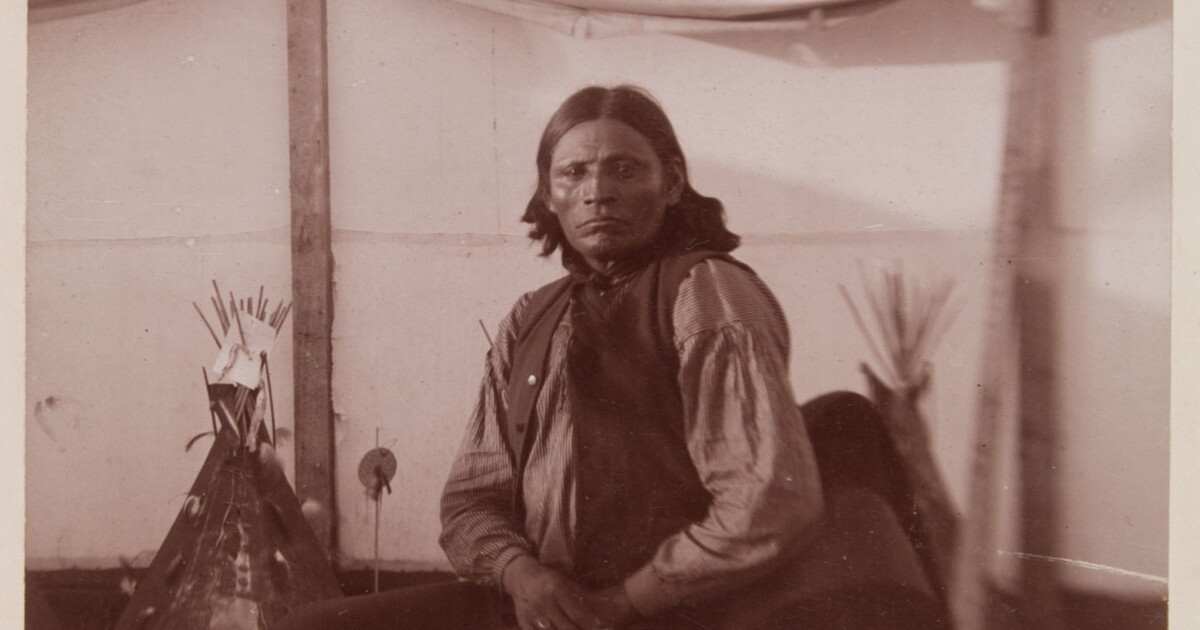 [Anko wearing striped shirt and seated in canvas corral, tipi models in